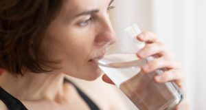 How Much Water Should You Drink Every Day? woman in black tank top drinking water