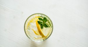 Health Secrets You Didn’t Know About Lemon Water filled clear drinking glass with sliced citrus and green leaf vegetable